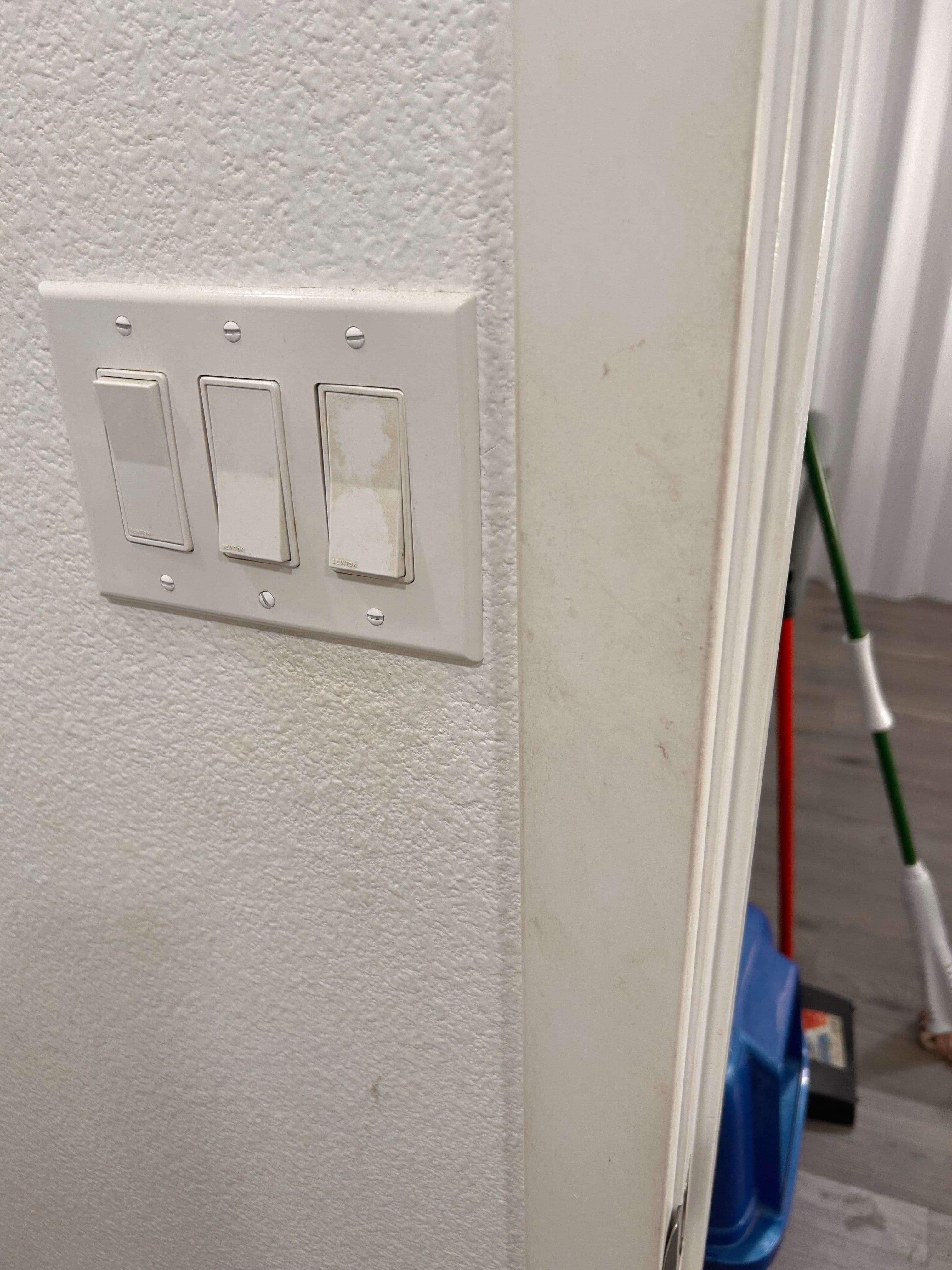 Three toggle light switches mounted on a textured white wall, near a doorway.
