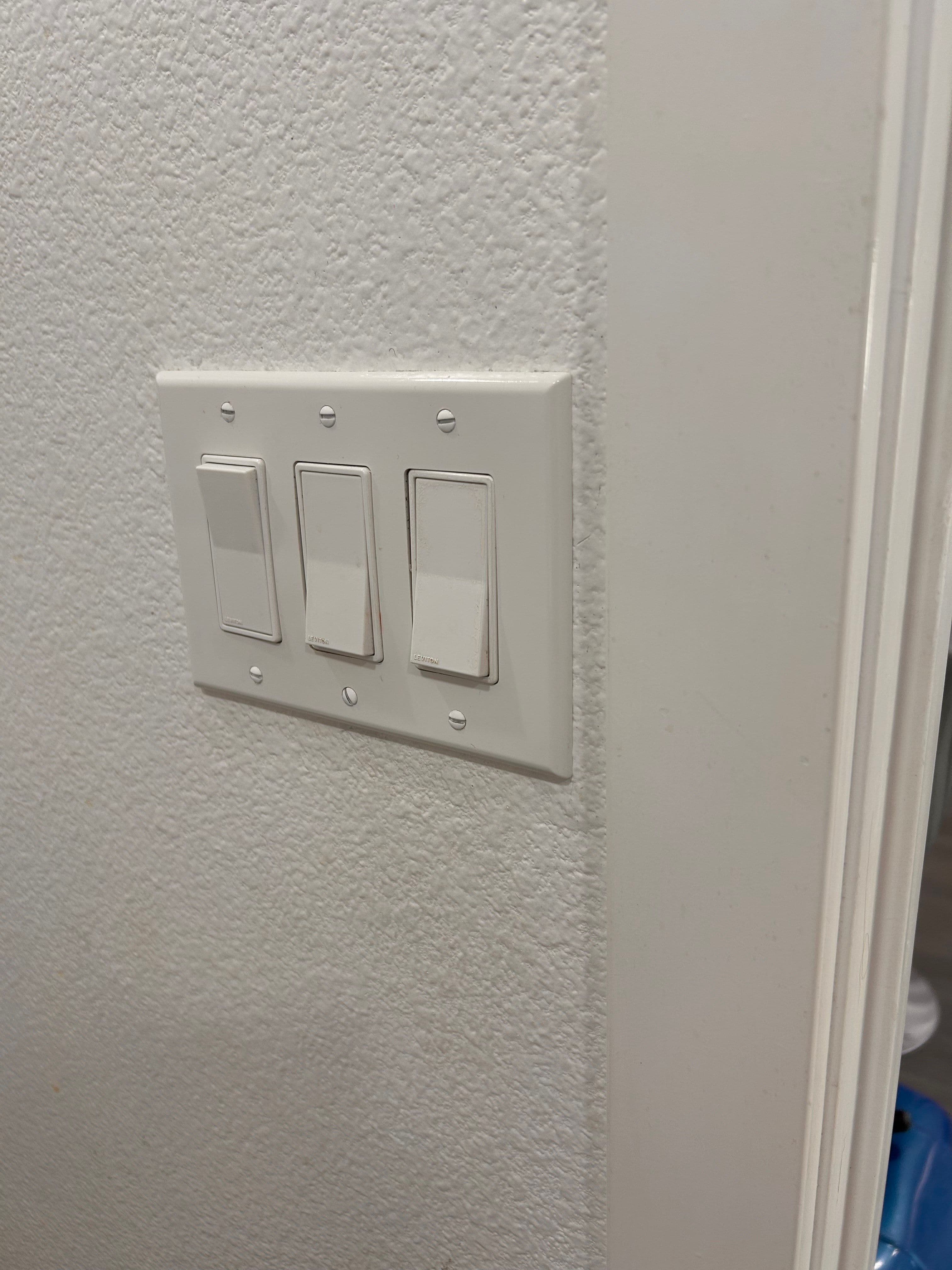 Three light switches mounted on a white wall near a doorway.